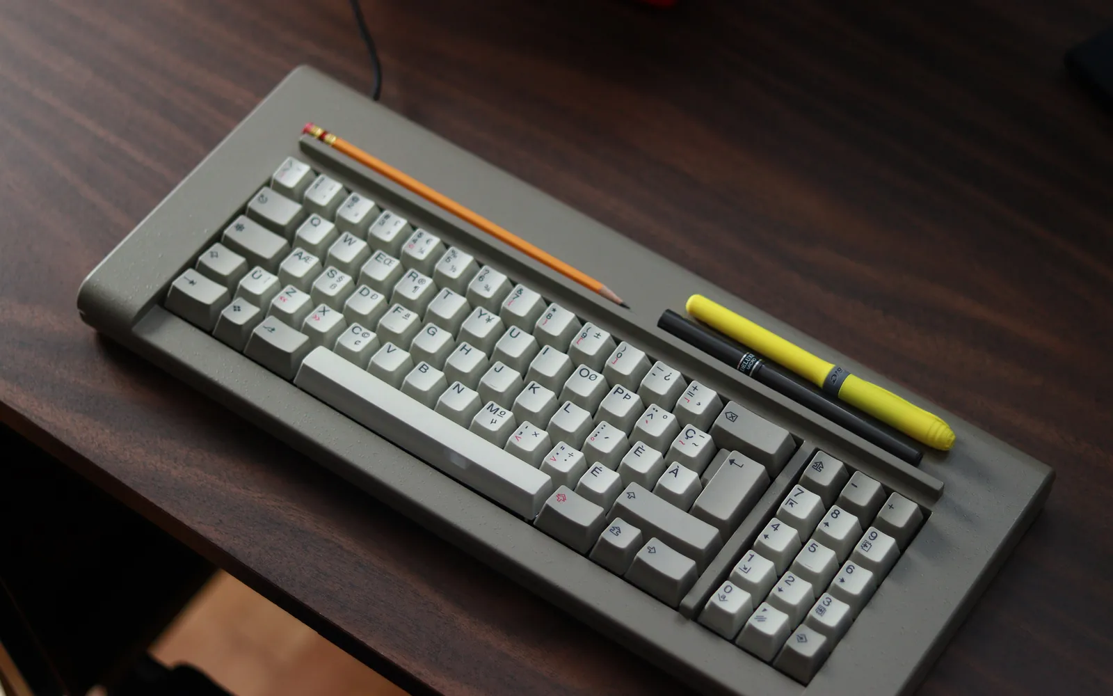 A compact keyboard on a dark wooden desk next to a pencil