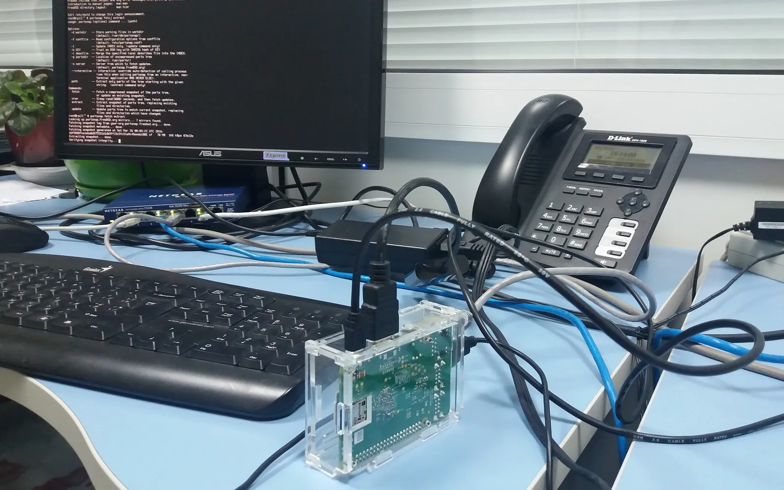 Un bureau avec un écran affichant un terminal, un clavier et des câbles