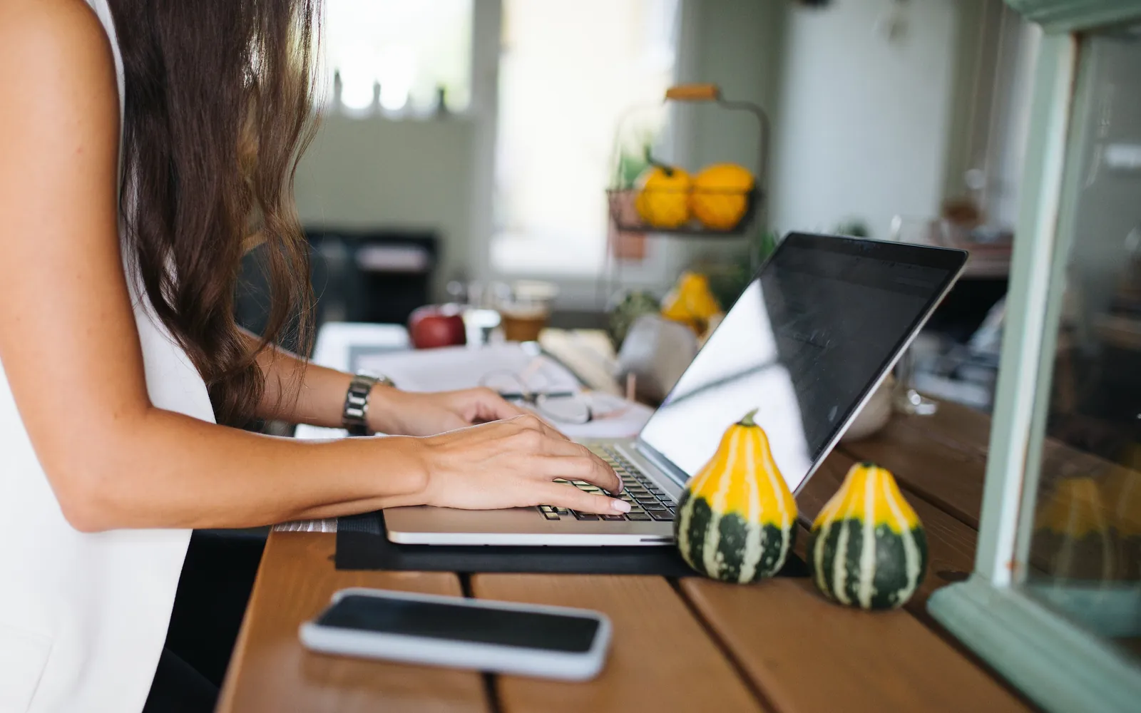 A woman typing on a laptop at a wooden kitchen table