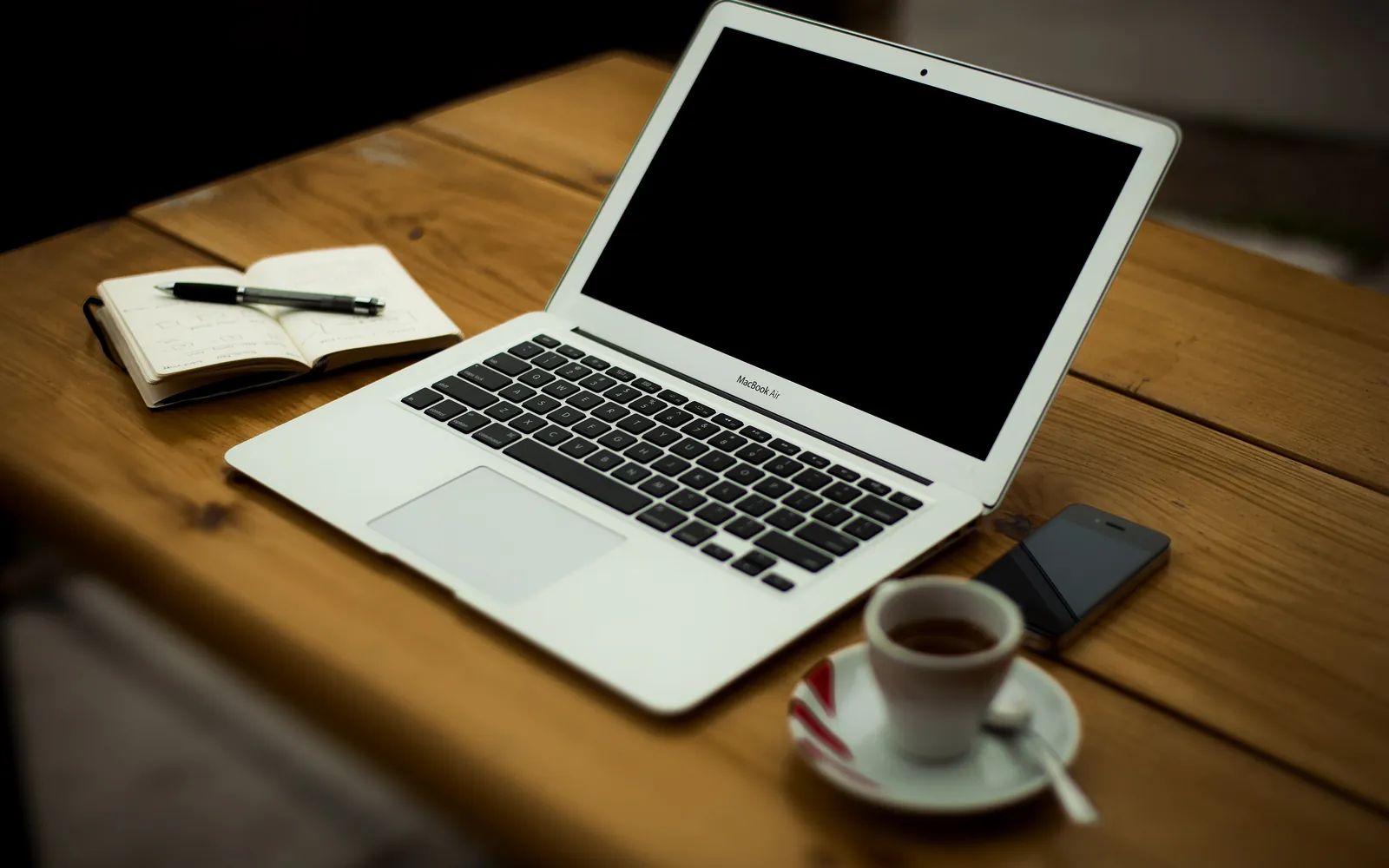 Un portátil, una libreta y una taza de café sobre un escritorio de madera